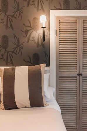 A bedroom with a bed, a striped pillow, a nightstand, a wall-mounted lamp, and a wooden wardrobe.