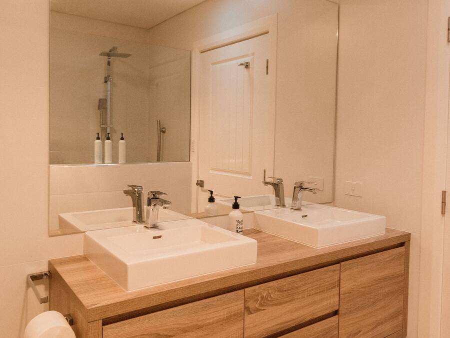 Une salle de bain avec deux lavabos, un grand miroir et un meuble-lavabo en bois.
