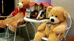 A room with a large bear cutout on the wall, two teddy bears on chairs, and a shelf with smaller stuffed animals. - Little Bear Guesthouse and Restaurant (Hat Yai)