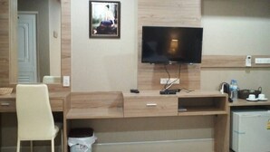A compact hotel room with a wooden desk, a television mounted on the wall, a small refrigerator, and a trash bin. - Little Bear Guesthouse and Restaurant (Hat Yai)