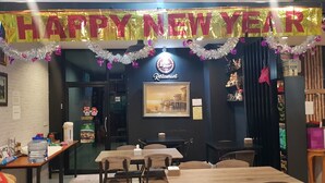 A restaurant with a 'Happy New Year' banner, a sign indicating a restaurant, and a framed picture on the wall. - Little Bear Guesthouse and Restaurant (Hat Yai)