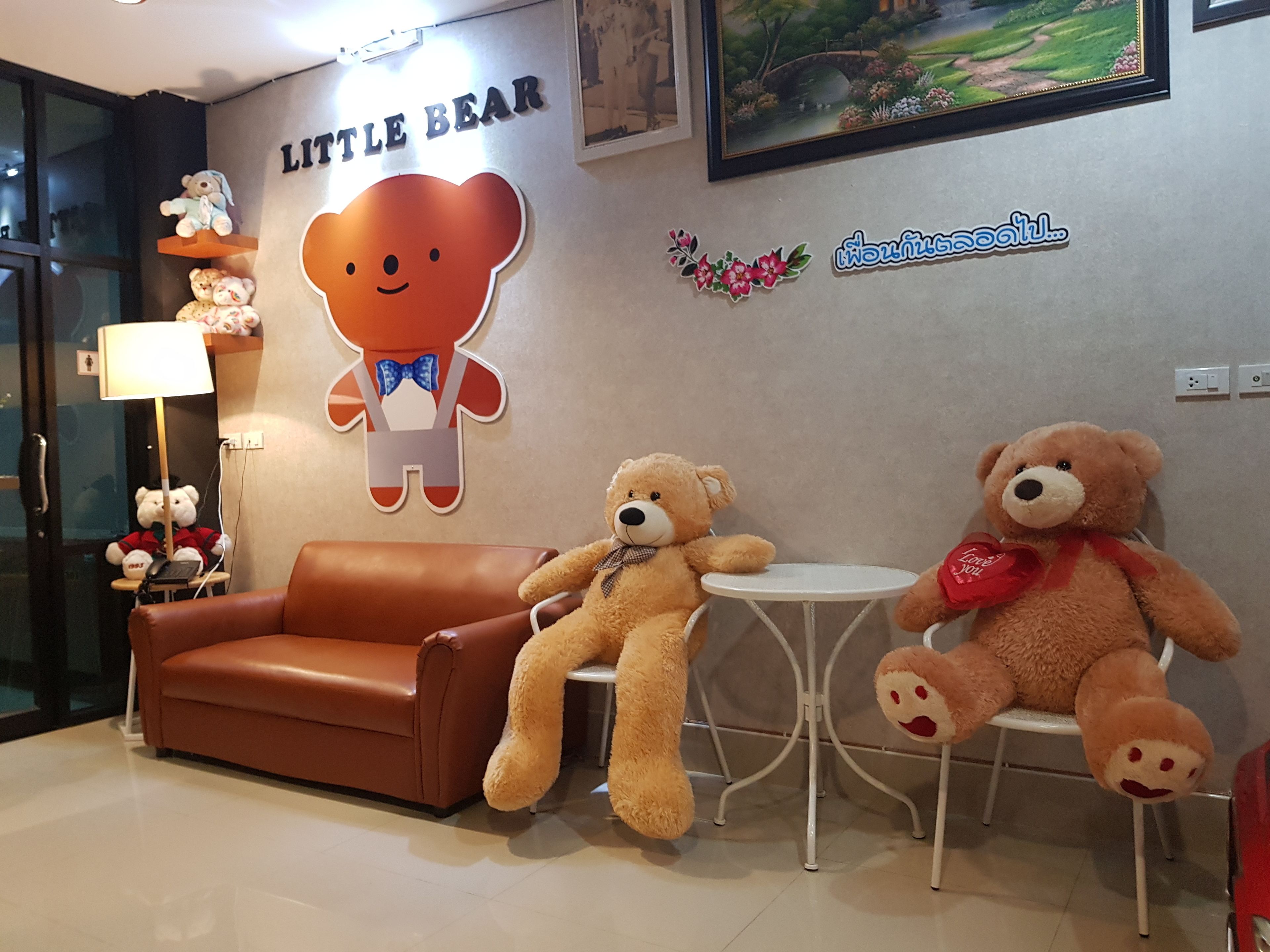 Habitació amb un sofà de cuir marró, dos óssos de peluix, una taula rodona petita i una paret amb un cartell que diu 'Little Bear'.