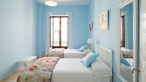 Une chambre avec deux lits, une fenêtre avec des rideaux, une table de chevet, une lampe et un miroir.