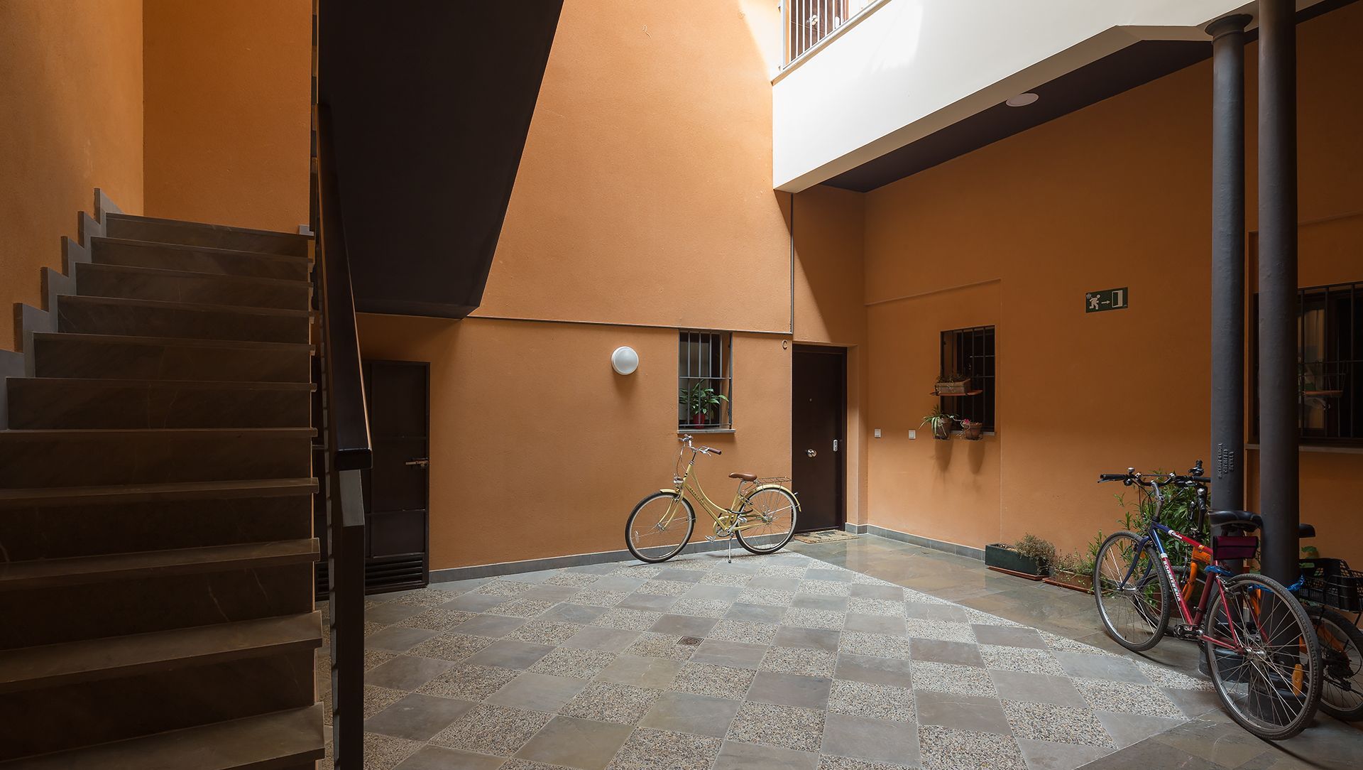 Amplio espacio interior con una escalera que conduce a un nivel superior, suelo de baldosas y bicicletas apoyadas contra las paredes.