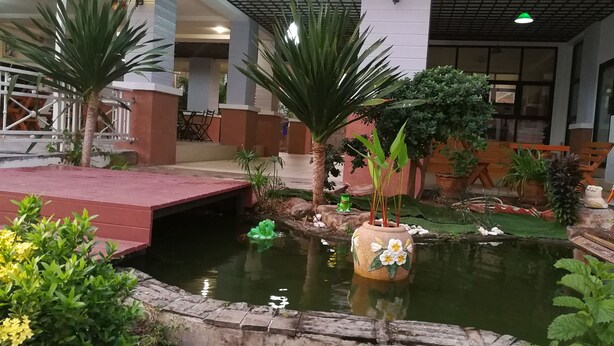 Um jardim interno com lago, palmeiras e um vaso de flores decorativo.