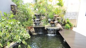 Un estanque de carpas con cascada, rodeado de exuberante follaje y una terraza de madera.