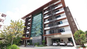 Un edificio de varios pisos con diseño moderno, destacándose por su fachada de vidrio y un área de estacionamiento con varios automóviles.