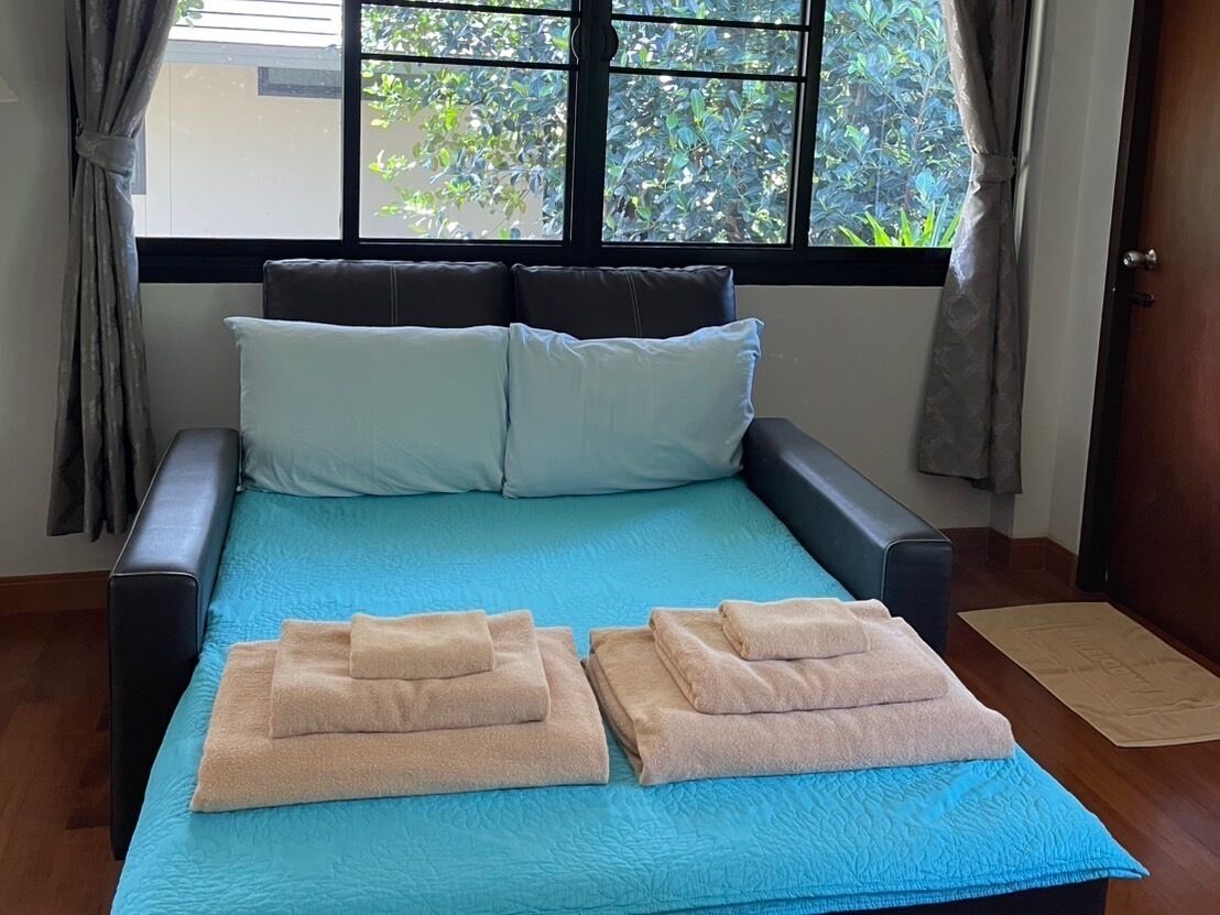 Una cama con cubrecama azul, dos toallas color beige y una ventana con cortinas.