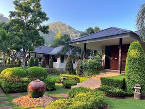 A modern resort with a well-maintained garden, a large decorative water feature, and a mountain backdrop. - Khaokhab Lodge (Pak Chong)