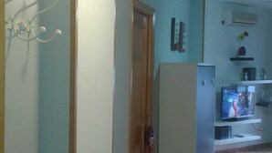 Un pasillo con una puerta, un refrigerador y un televisor al fondo.