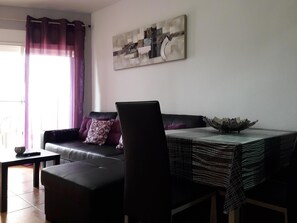 Ein Wohnzimmer mit einer Couch, einem Esstisch mit gemustertem Tischläufer und einem Bild an der Wand.