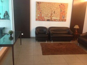 Un salon avec deux canapés en cuir noir, une table basse en verre, un tapis marron et un grand tableau abstrait accroché au mur.
