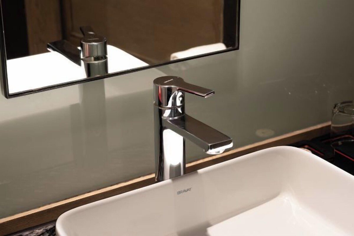 Une salle de bain avec un lavabo blanc, un robinet chromé et un miroir qui reflète le robinet.