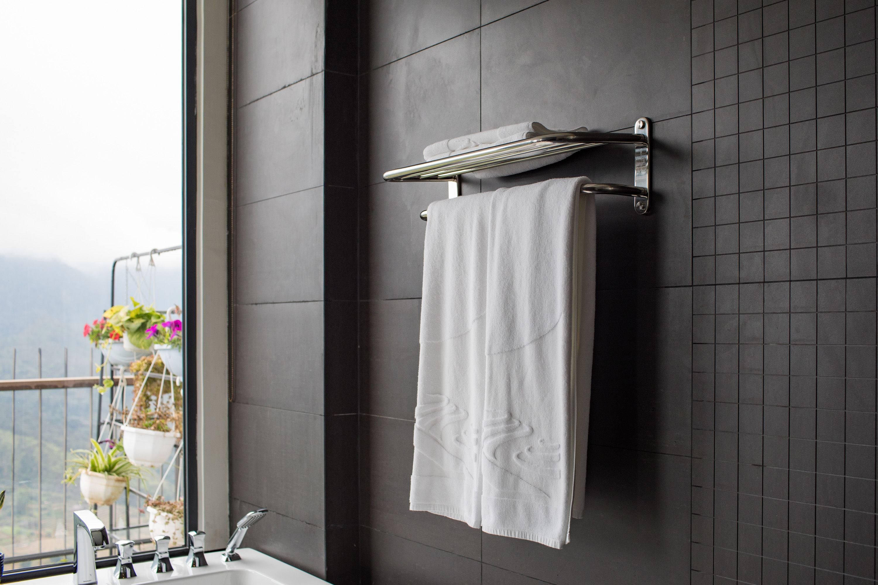 A bathroom with a large window, a towel rack with a white towel, and a sink with a faucet.
