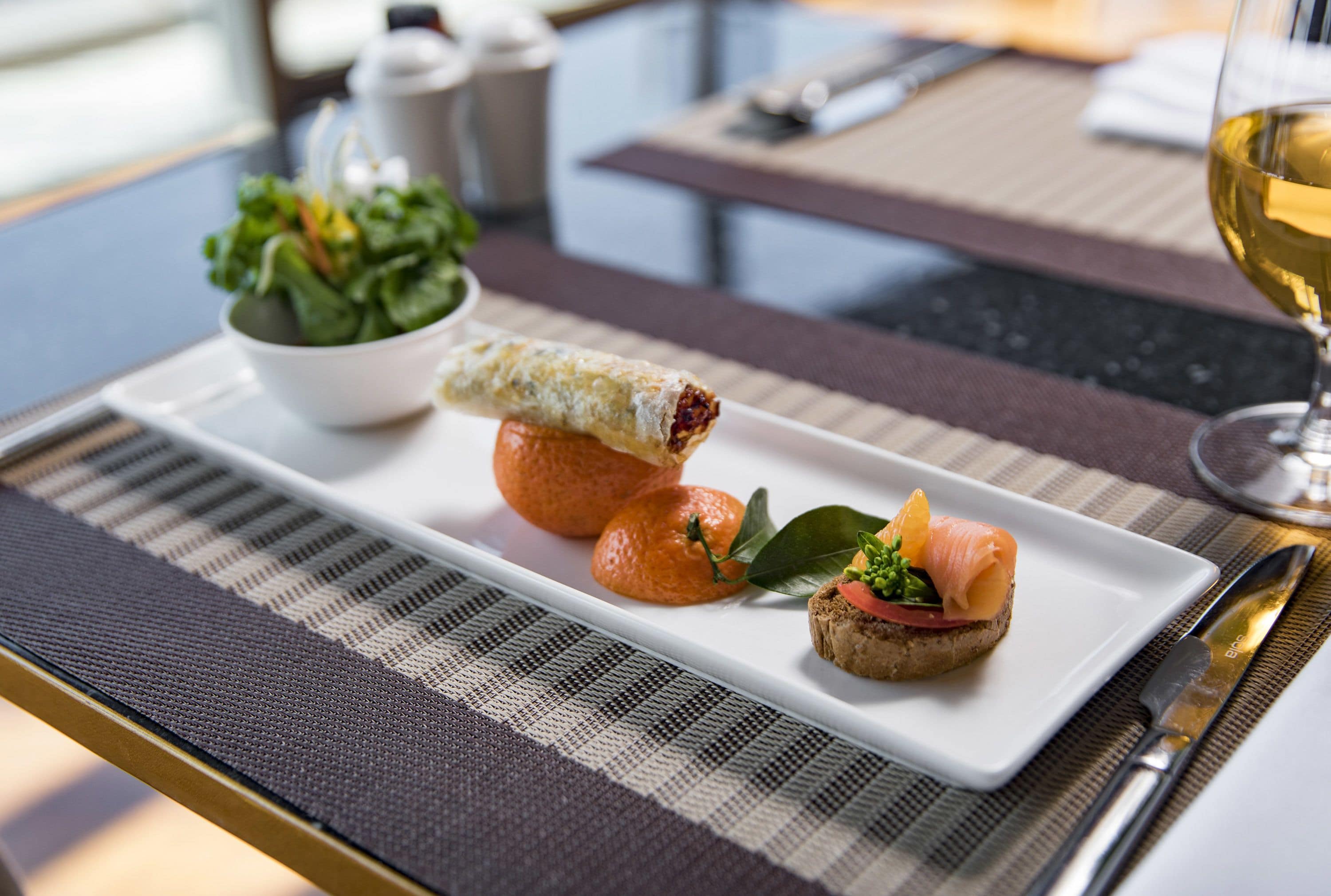 A dining table with a plate of food, a bowl of salad, and a glass of wine.