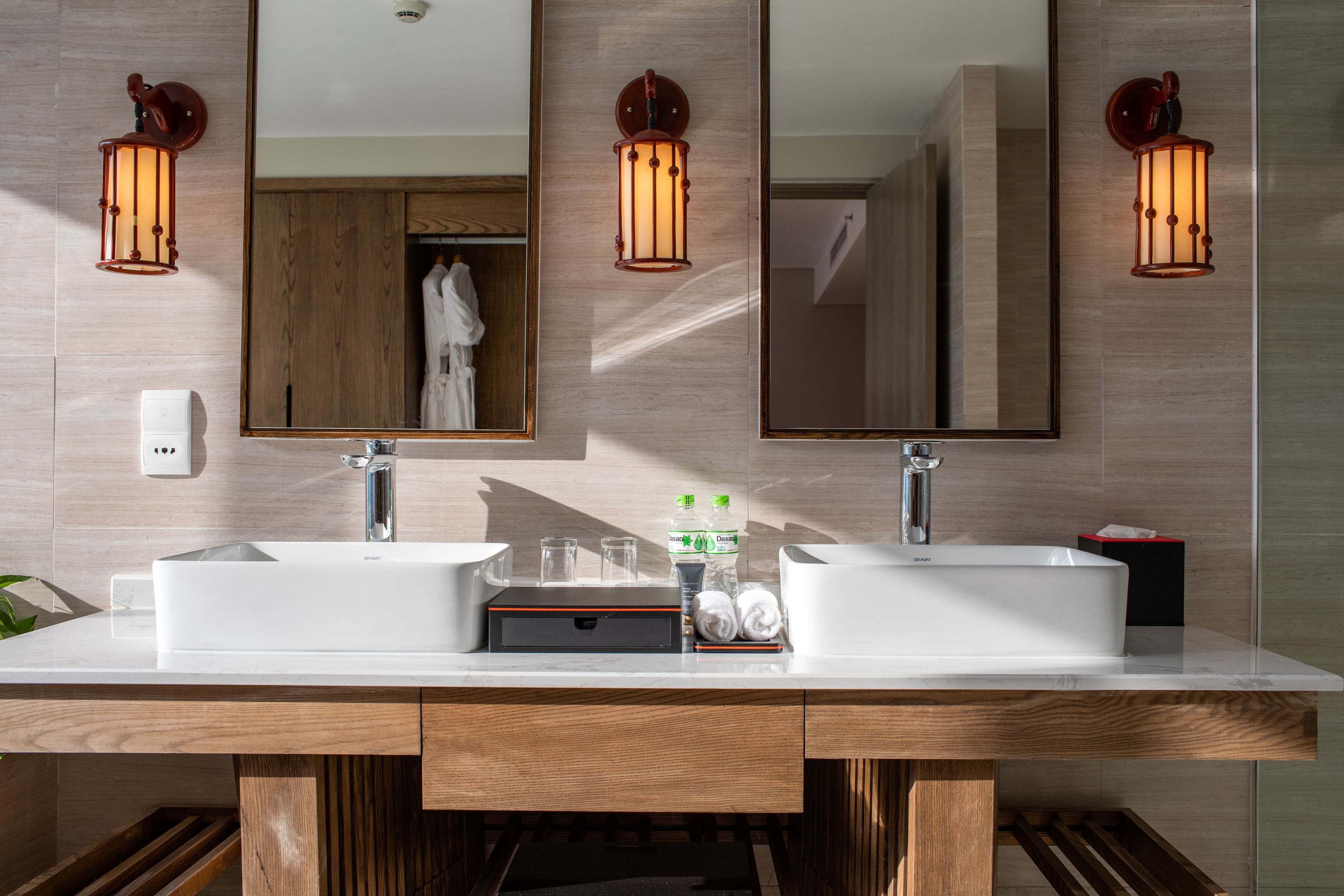 A modern bathroom with a double sink, wooden vanity, and three wall-mounted sconces.