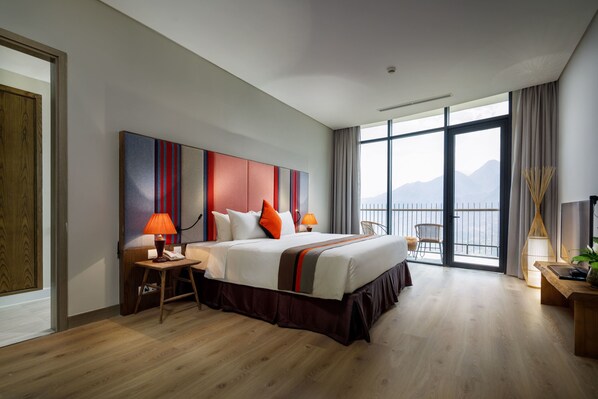 Une chambre d’hôtel moderne dotée d’un grand lit, d’un bureau, d’une chaise et d’un balcon offrant une vue sur les montagnes.