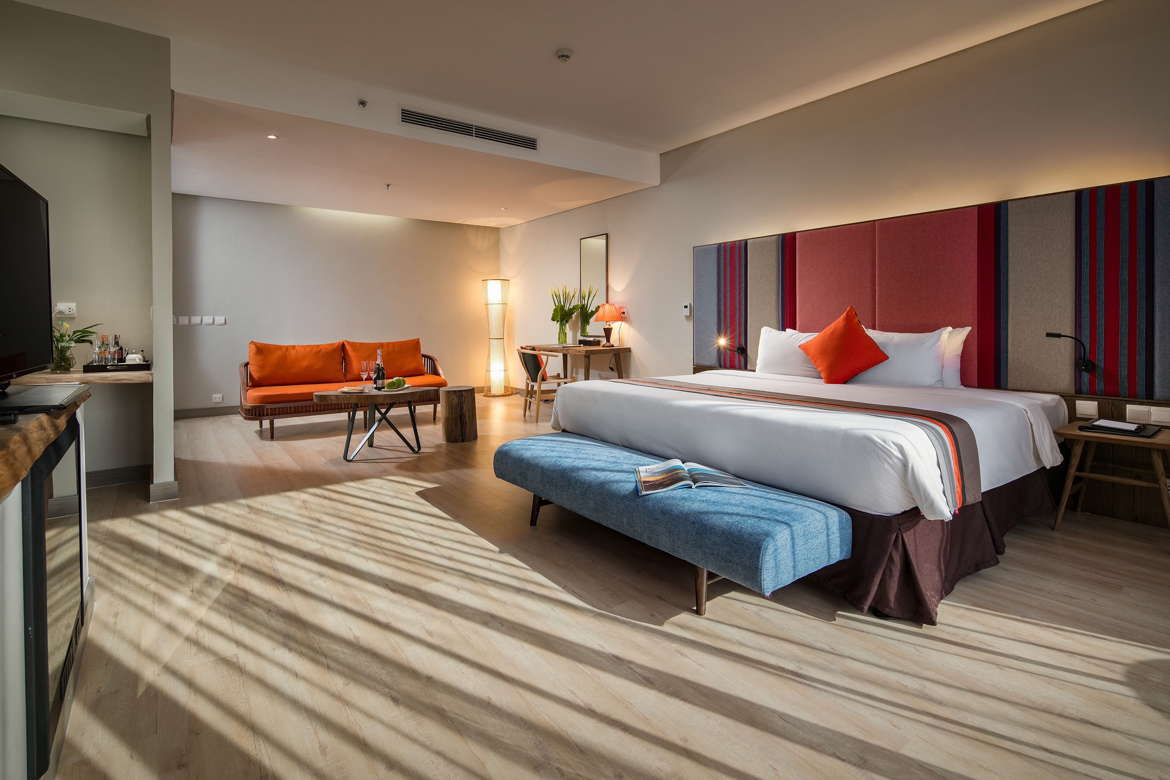 Een moderne hotelkamer met een groot bed, een slaapbank, een bureau en een lamp.