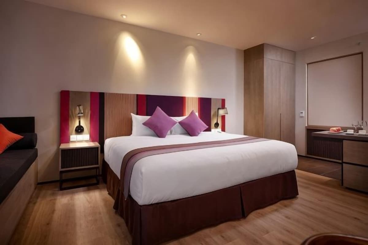 A modern hotel room with a large bed, bedside tables, a desk, and a wardrobe.