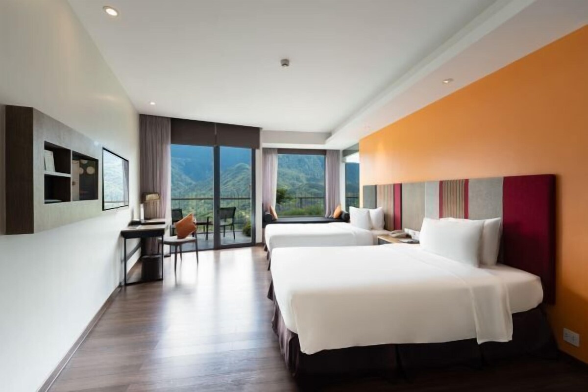 Een hotelkamer met twee bedden, een bureau en een balkon met uitzicht op de bergen.