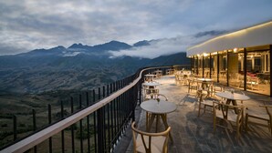 Terraço com mesas e cadeiras com vista para uma paisagem montanhosa.
