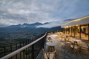 Eine Terrasse mit Tischen und Stühlen mit Blick auf eine gebirgige Landschaft.