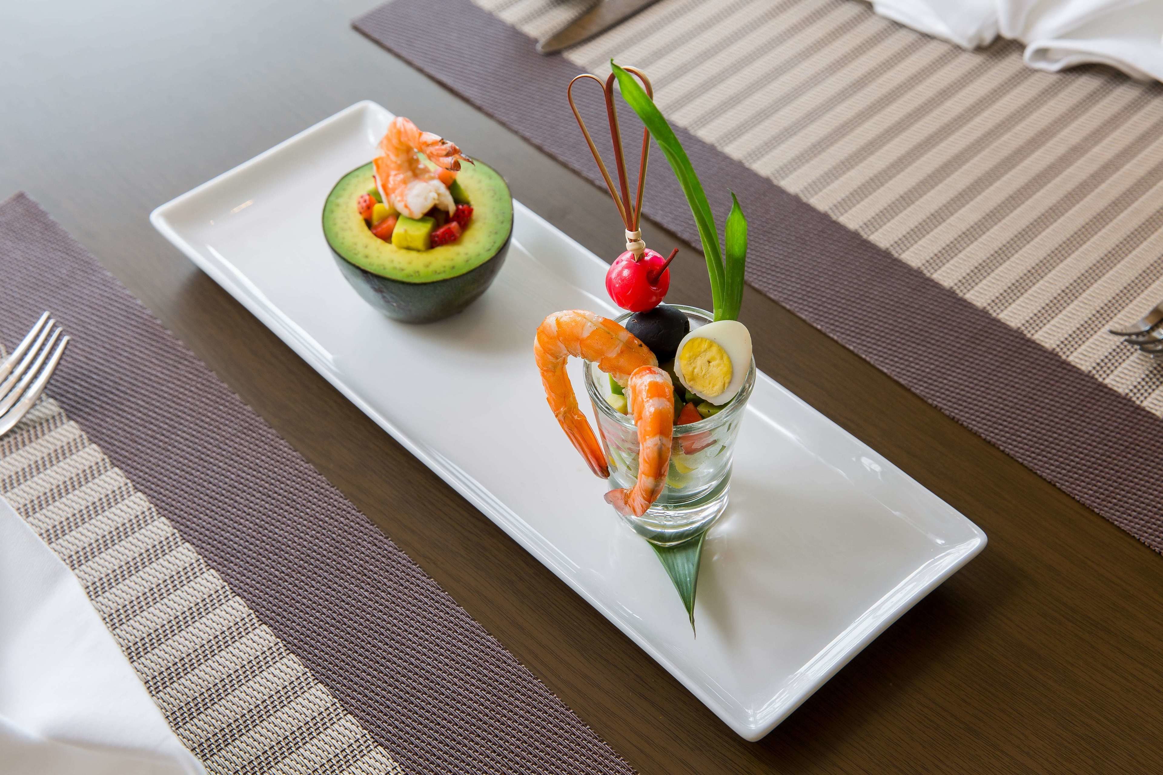 A dining table with a white plate containing a salad, a shrimp, and a decorative item.