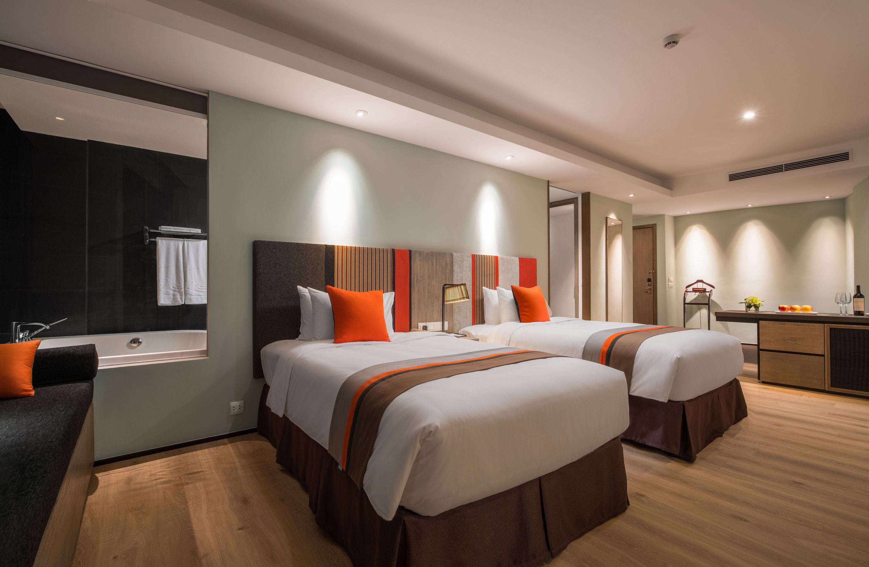 A modern hotel room with two beds, a large window, a bathroom, and a kitchenette.