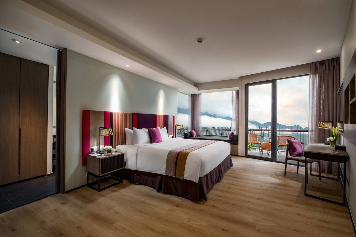 Ein modernes Hotelzimmer mit einem großen Bett, einem Schreibtisch und einem Balkon mit Bergblick.