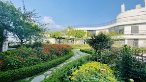 A modern building with a curved facade, surrounded by well-maintained gardens with various plants and flowers.