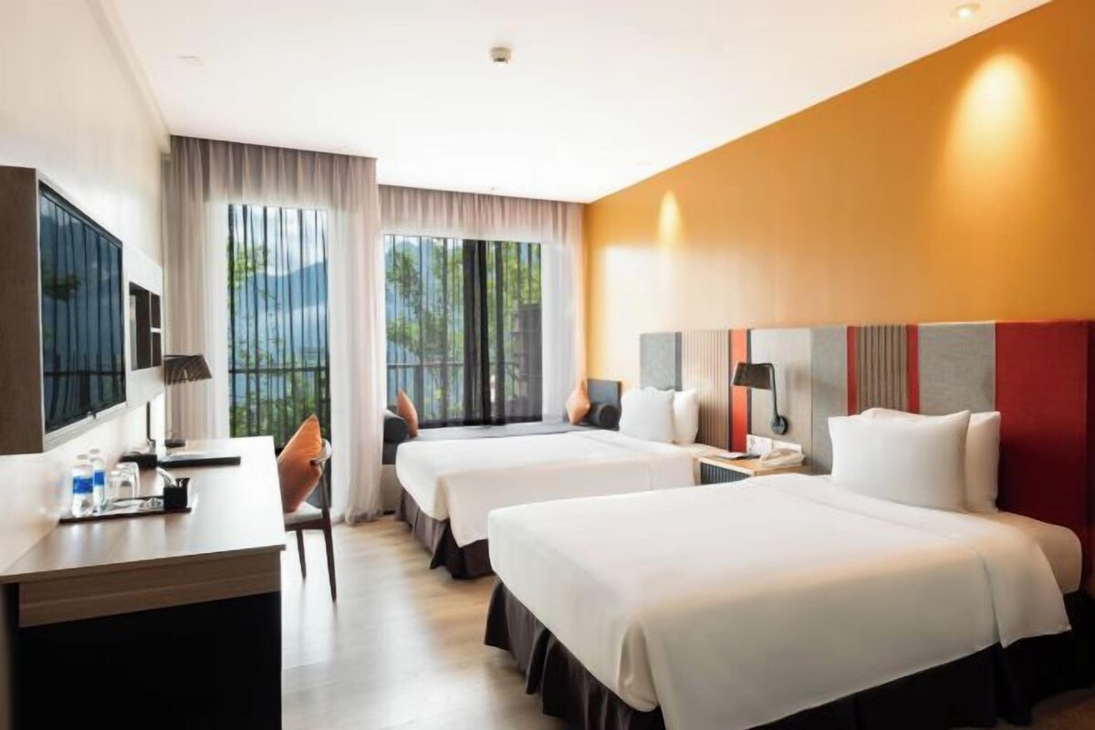 Une chambre d’hôtel avec deux lits, un bureau, une chaise, une télévision et une fenêtre avec des rideaux.