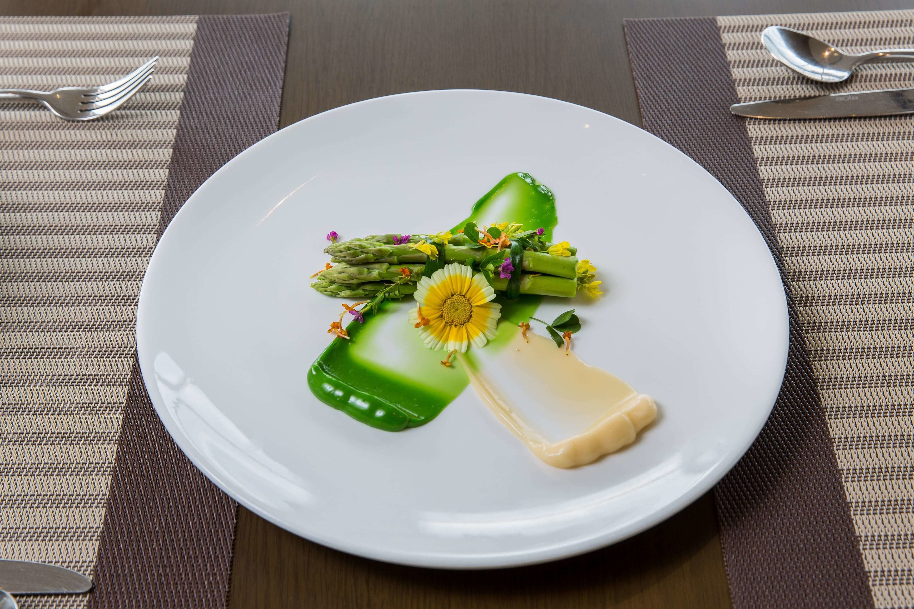 A white plate with a green vegetable, a yellow flower, and a piece of cheese.