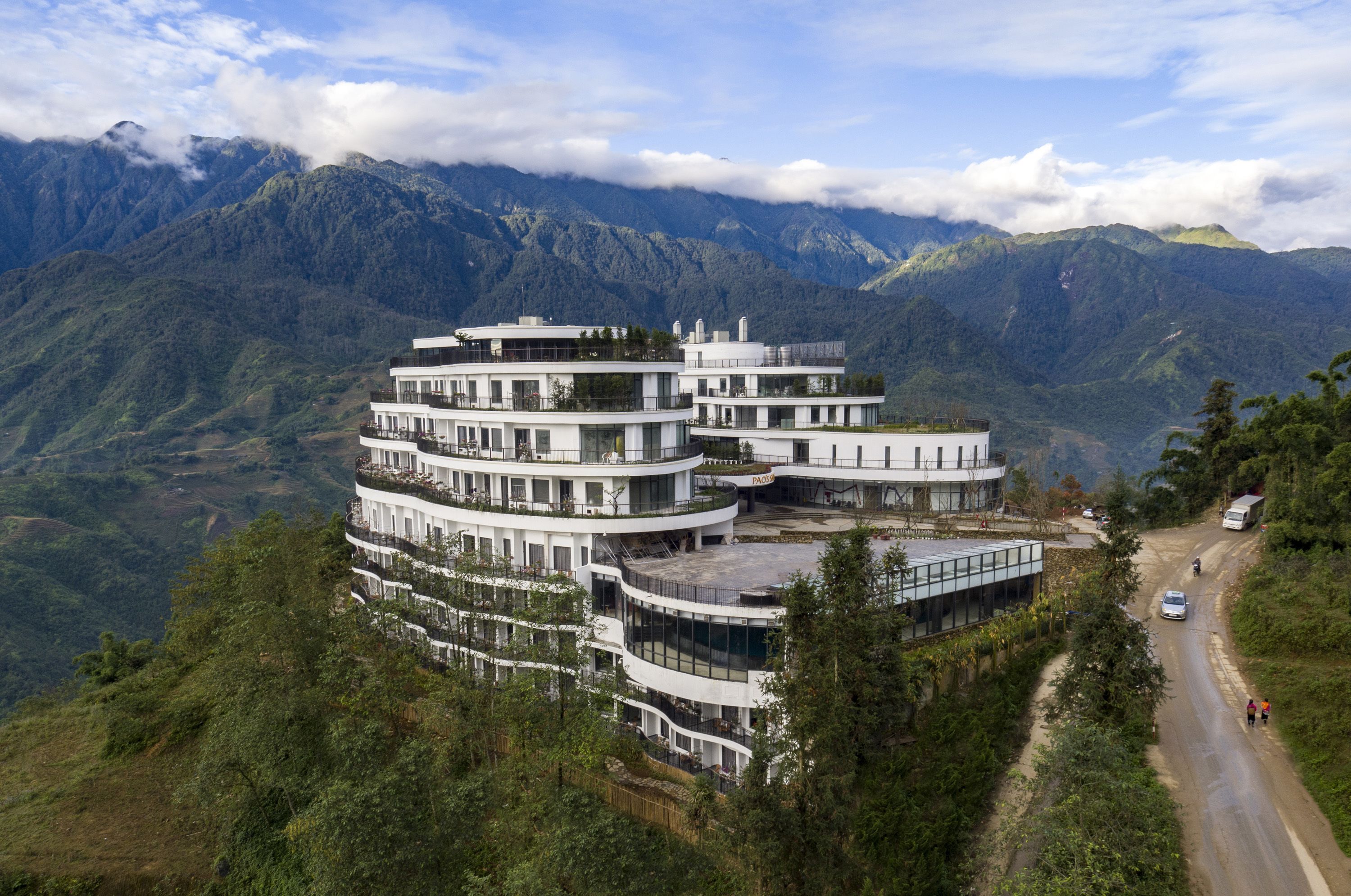 Un hotel de varios pisos con una arquitectura curva distintiva, ubicado en una ladera con vistas a la montaña.