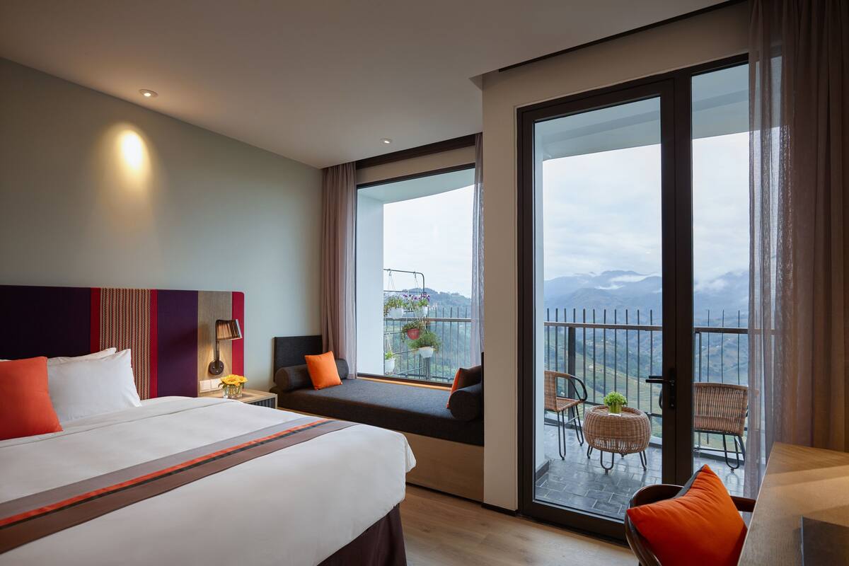 Ein Hotelzimmer mit einem großen Bett, einer Couch, einem Balkon mit Bergblick und einem Essbereich mit Stühlen.