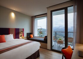 Habitación de hotel con una cama grande, un sofá, un balcón con vistas a las montañas y un comedor con sillas.