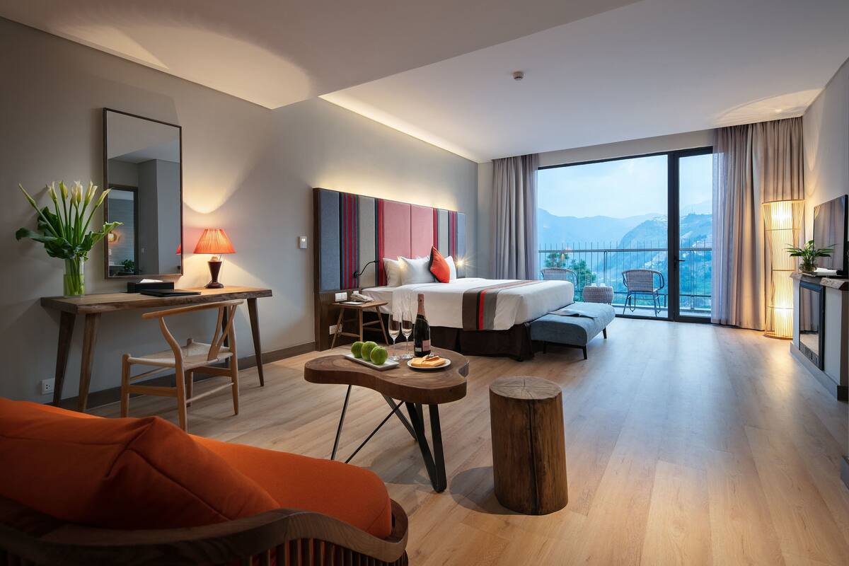 Ein modernes Hotelzimmer mit einem großen Bett, einem Schreibtisch, einem Sessel und Blick auf die Berge.