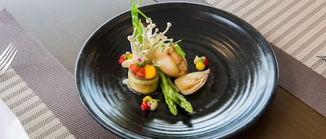 A black plate with a scallop, asparagus, and small vegetables on a table with a striped placemat.