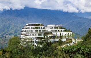 A multi-story hotel with balconies, set against a mountainous backdrop.