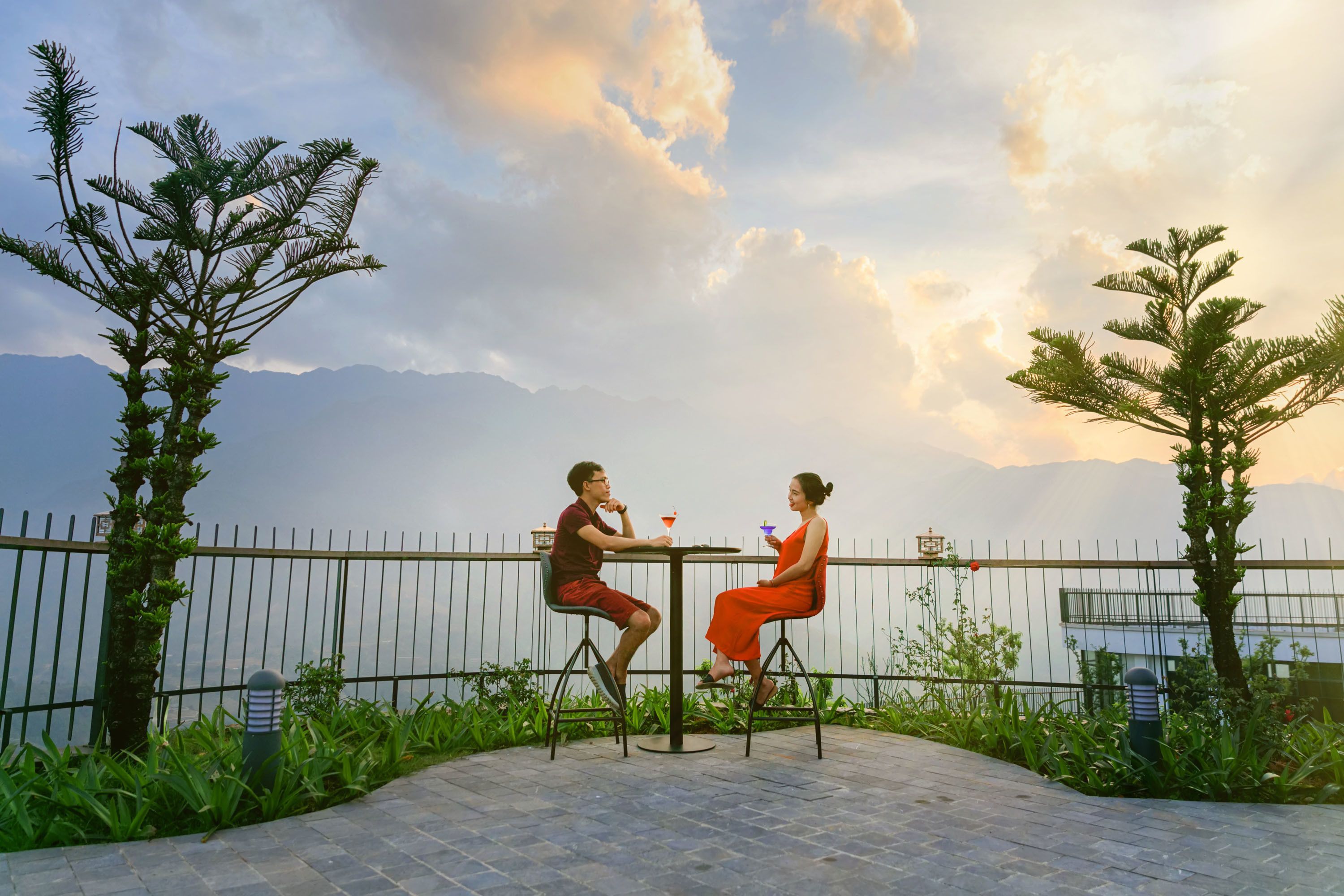 Two people seated at a table outdoors with a view of mountains and a fence in the background.