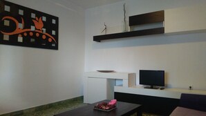 Un salon moderne avec un téléviseur à écran plat, une petite table sur laquelle est posé un vase de fleurs et un élément décoratif mural.