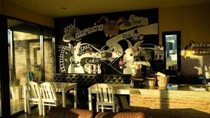 A cozy dining area with a mural, a brick wall, and a modern kitchen in the background. - Rabbit Hill Cafe and Resort @ Khao Yai (Pak Chong)
