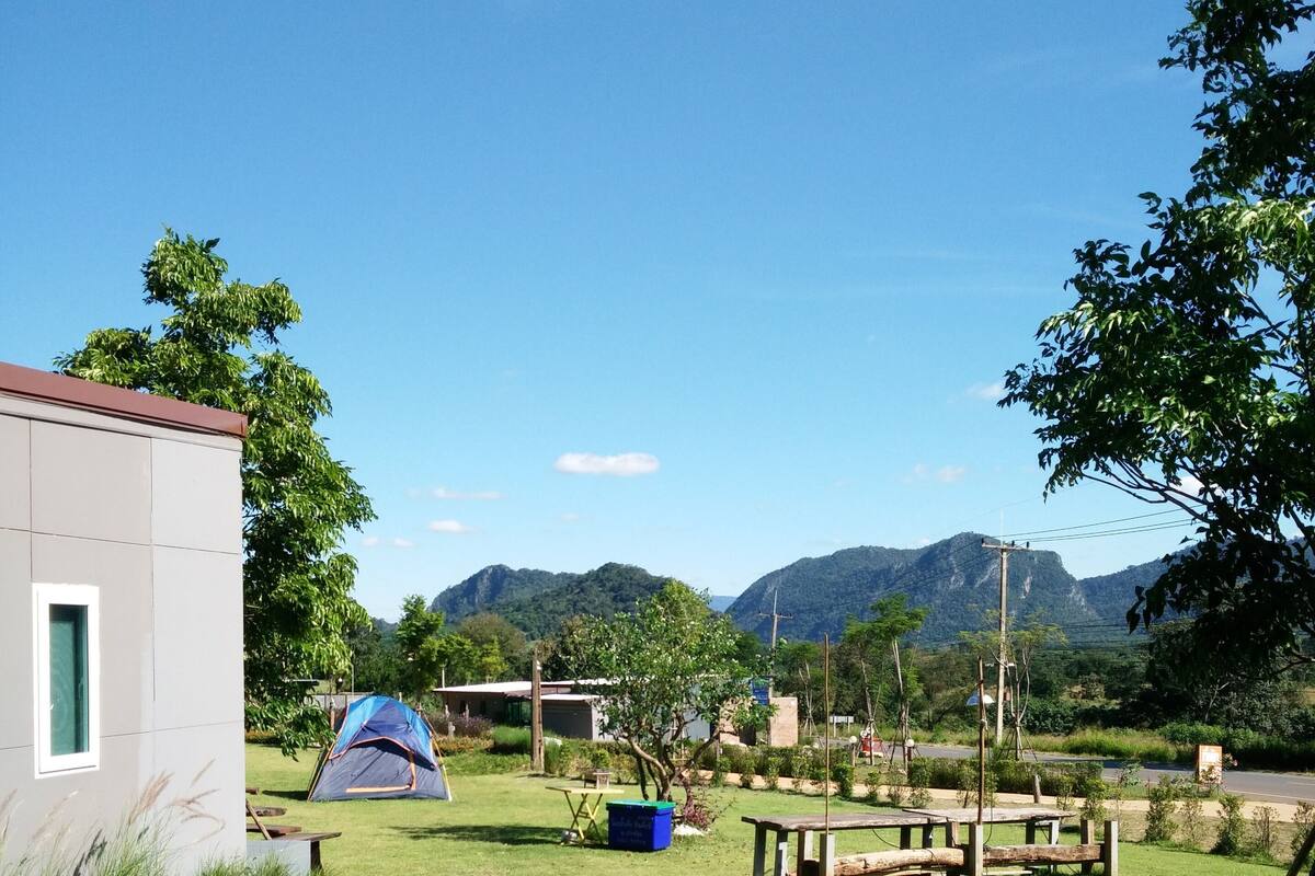 A campsite with a tent, picnic tables, and a building.