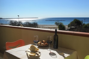 A table with a bottle of wine, glasses, bread, and cheese on a balcony overlooking a beach. - The Romantic Sunset apartment offers you an unforgettable view of the sea (Alghero)