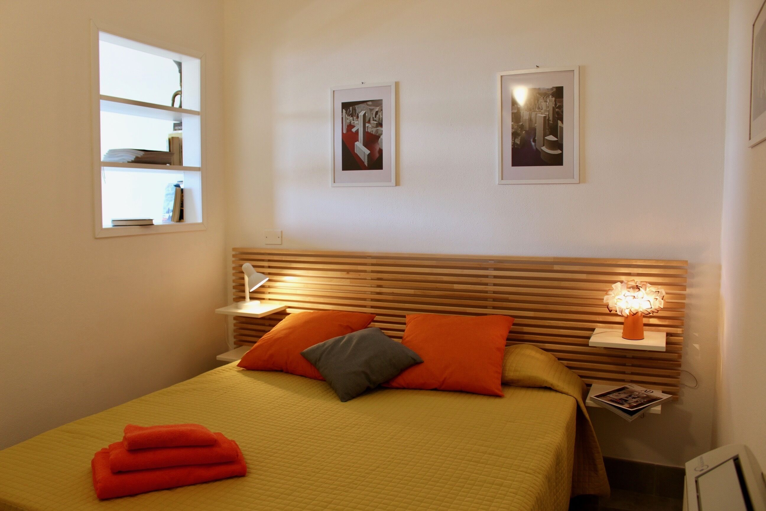 A neatly arranged bedroom with a bed, pillows, bedside tables, and wall-mounted shelves.