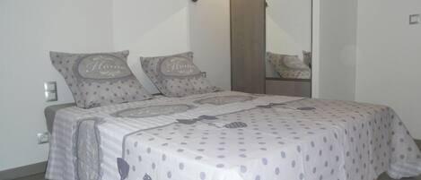 A bedroom with a bed covered in a polka dot bedspread, two pillows with the word "Home" on them, a wooden door, and a mirror on the wall.