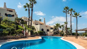 Una piscina rodeada de palmeras y un edificio de estilo arquitectónico mediterráneo.