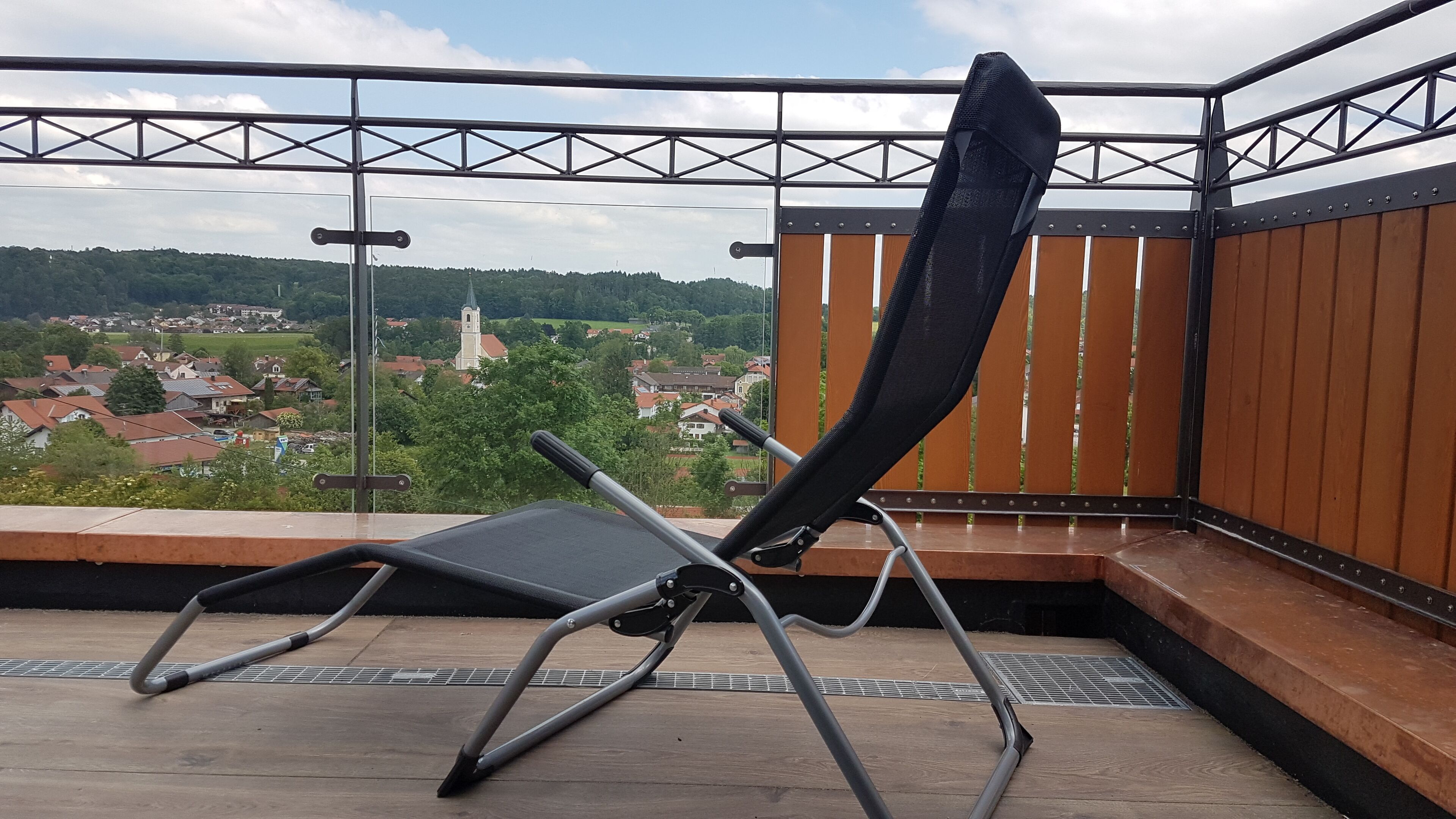 Un balcon avec une chaise en métal et une vue sur une ville avec des maisons et une église.