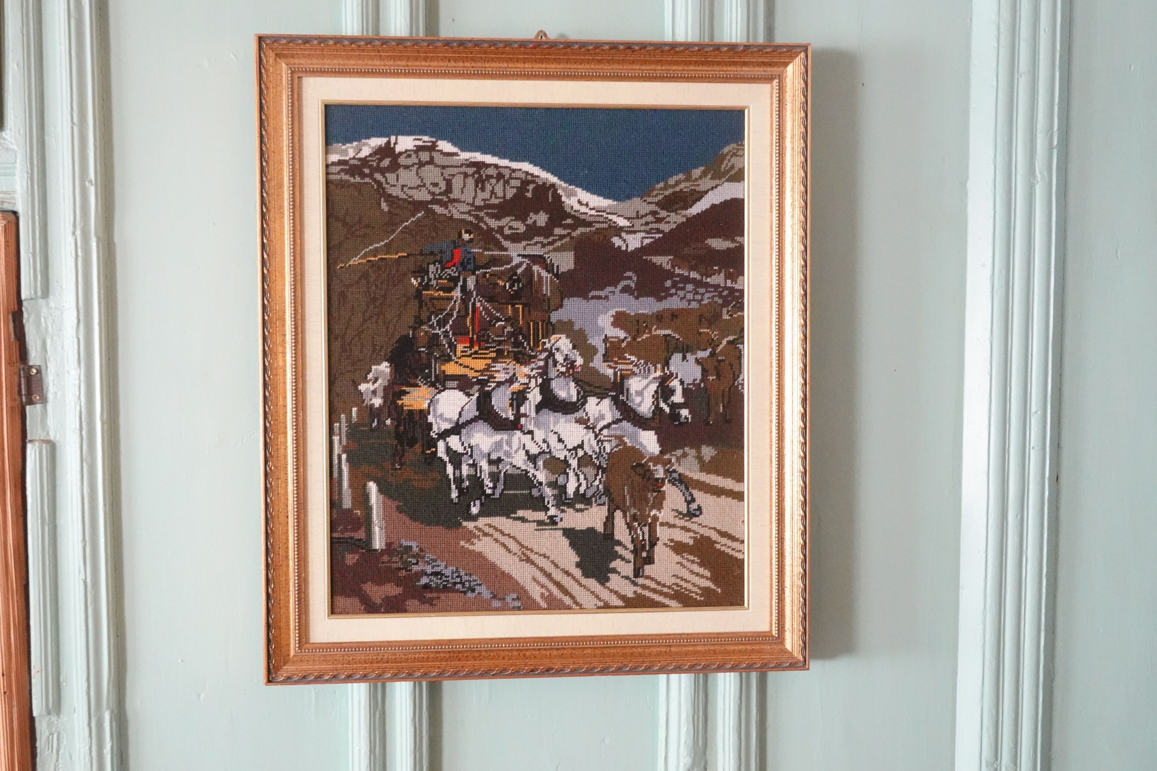 Une œuvre d’art encadrée représentant un paysage montagneux avec un groupe de chevaux et de cavaliers.