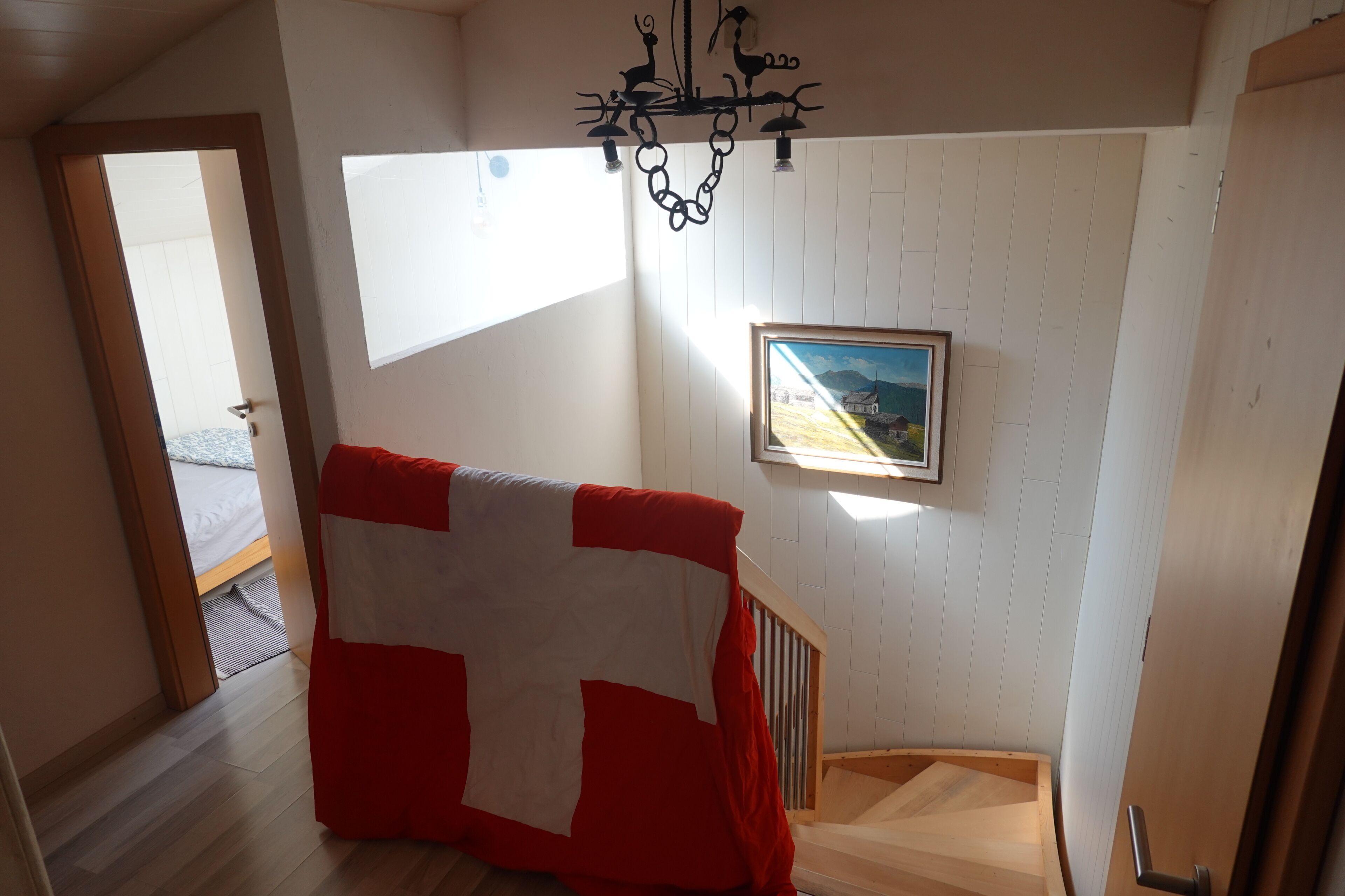 A staircase with a wooden handrail, a red and white blanket draped over it, and a framed painting on the wall.