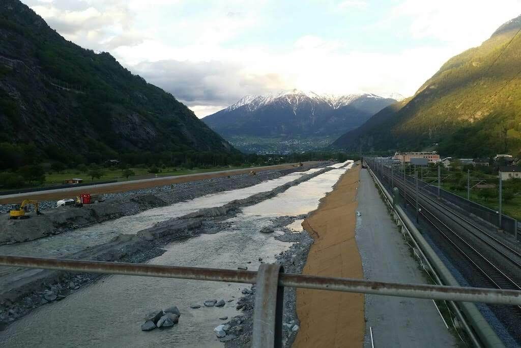 Un chantier de construction avec une voie ferrée, des montagnes en arrière-plan et un pont en construction.